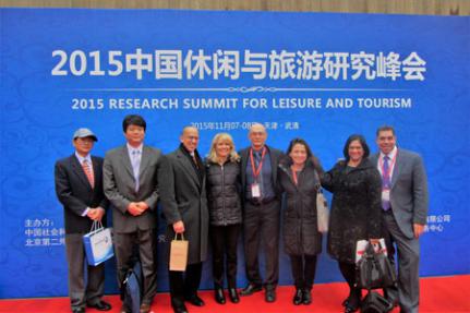 8 people standing in front of curtain with English and Chinese text reading 2015 Research Summit for Leisure and Tourism